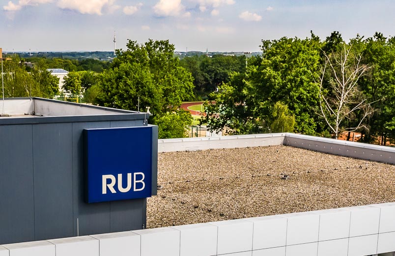 Das Foto zeigt das Dach des Fakultätsgebäudes mit dem blauem RUB-Würfel
