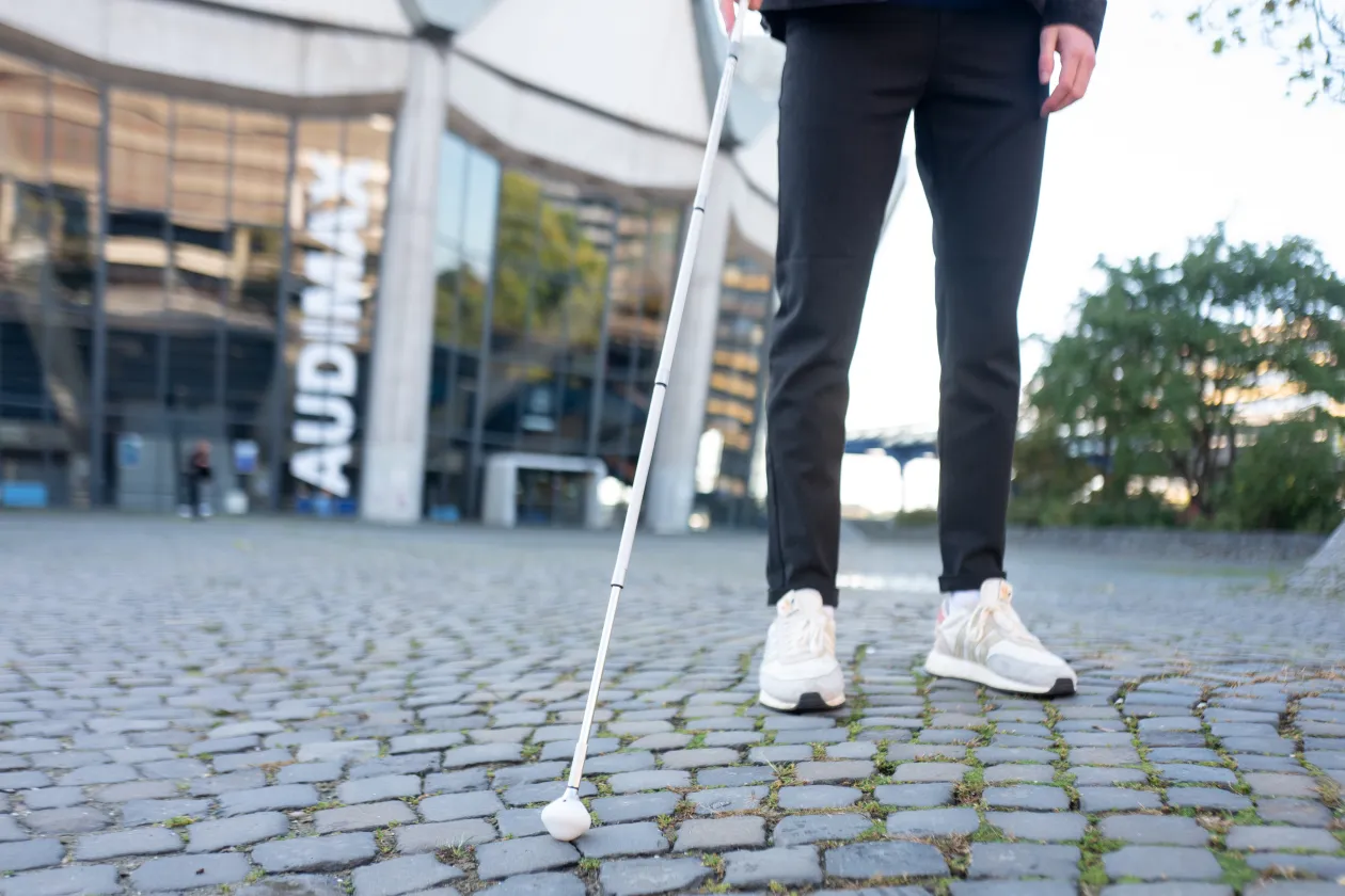 Blinder mit Blindenstock auf dem Kopfsteinpflaster des Forums vor dem Audimax