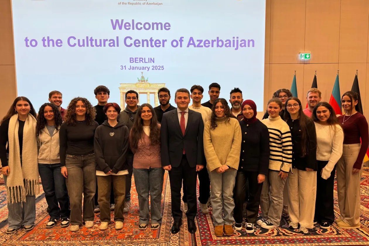 Foto: Gruppe von Schülerinnen und Schülern des TalentKollegs Ruhr Hagen mit dem Botschafter der Republik Aserbaidschan in Deutschland in der Mitte. Im Hintergrund ist eine projizierte Präsentation zu sehen mit dem Titel "Welcome to the Cultural Center of Azerbaijan; Berlin, 31 January 2025".