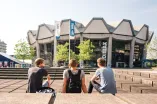 Drei Studierende sitzen vor dem Audimax der Ruhr-Unviersität.