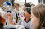 Ein Schüler wird von einem Roboterarm an der Nase berührt.
