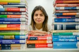 Eine Studierende über einem Stapel Bücher.