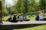 Foto: Studierende sitzen auf einer Wiese und auf Steinen. Man sieht nur die Rücken der Personen.