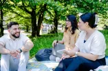 Drei junge Menschen sitzen auf einer Wiese und unterhalten sich