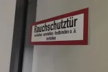 The sticker on a door with the notice "Smoke protection door. wedging, adjusting, tying down or similar prohibited