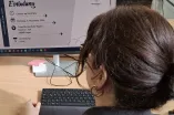 Frau in Büro schaut auf die geöffnete Einladung zur Veranstaltung auf ihrem PC