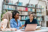 Drei Studentinnen sitzen in der Biblitohek und schauen auf einen Laptop
