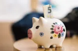 Foto: Ein Sparschwein mit Blumenmuster. Oben guckt ein 5 Euro-Schrein raus.