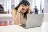 Studentin sitzt vor einem Laptop. Ihren Kopf hat sie in ihre Hände gelegt.