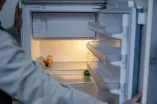 Blick über die Schulter einer Person auf einen leeren, geöffneten Kühlschrank. 