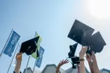 Foto: Das Bild zeigt viele Hände, die Absolventenkappen in die Luft werfen, im Hintergrund RUB-Flaggen und das Dach vom Audimax.