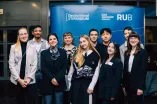 Photo: Several people are standing in front of a blue display stand, smiling. The display stand features the logos of the Deutschlandstipendium and Ruhr University Bochum.