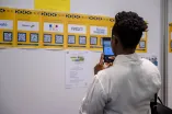 Person steht mit Handy vor einer Wand mit Jobaushängen