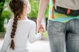 Das Foto zeigt von hinten eine Mutter und ihr Kind, die sich an den Händen halten