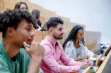 Studierende sitzen nebeneinander in einem Hörsaal, machen sich Notizen und folgen der Lehrveranstaltung.