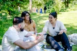 Das Foto zeigt zwei junge Frauen und einen jungen Mann die zusammen auf einer Decke auf einer Wiese sitzen und zusammen reden und lachen.
