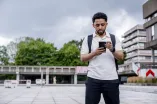Ein Student steht mit seinem Smartphone in der Hand auf dem Campusgelände der RUB.