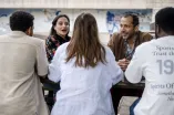 Das Bild zeigt fünf junge Menschen an einem Tisch auf dem RUB-Campus. Eine der beiden jungen Frauen erzählt etwas, alle hören ihr zu. 