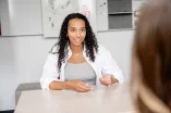 Das Fotos zeigt eine junge Frau in einer Gespächssituation, den Kopf ihres Gegenübers sieht man angedeutet von hinten im Bildvordergrund.