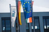 Das Foto zeigt verschiedenen Flaggen an Fahnenmasten vor einem Gebäude: Im Vordergrund die EU-Flagge, daneben Deutschland und RUB-Flagge, im Hintergrund verdeckt erahnt man noch die Landesflagge NRW
