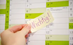 Hand klebt Post-it mit Aufschrift Wichtig auf einen Kalender.