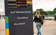 Studentin am Schild "Auf Wiedersehen/Goodbye/Au revoir" auf der Unibrücke"