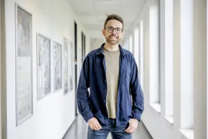 Der Projektkoordinator des Studentischen Gesundheitsmanagement, Peter Bickmann, steht vor einem hellen Flur im Uni-Gebäude SSC.