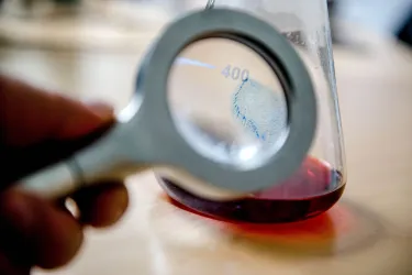 Mit einer Lupe wird ein Fingerabdruck auf einem Reagenzglas sichtbar.