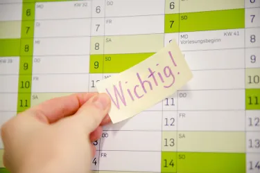 Hand klebt Post-it mit Aufschrift Wichtig auf einen Kalender.