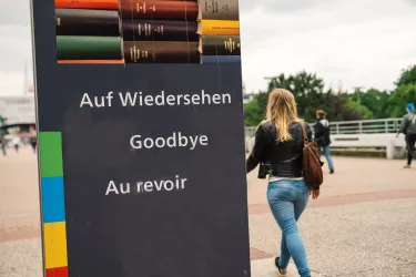 Studentin am Schild "Auf Wiedersehen/Goodbye/Au revoir" auf der Unibrücke"