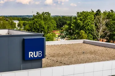 Das Foto zeigt das Dach des Fakultätsgebäudes mit dem blauem RUB-Würfel