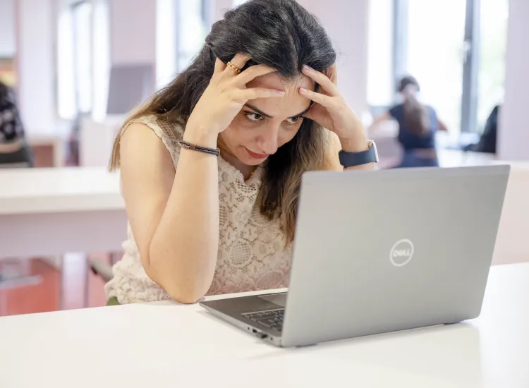 Studentin sitzt vor einem Laptop. Ihren Kopf hat sie in ihre Hände gelegt.
