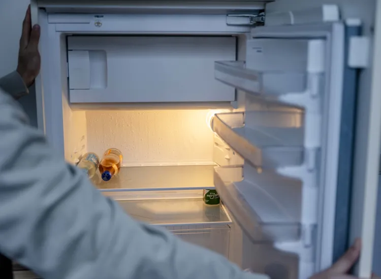 Blick über die Schulter einer Person auf einen leeren, geöffneten Kühlschrank. 