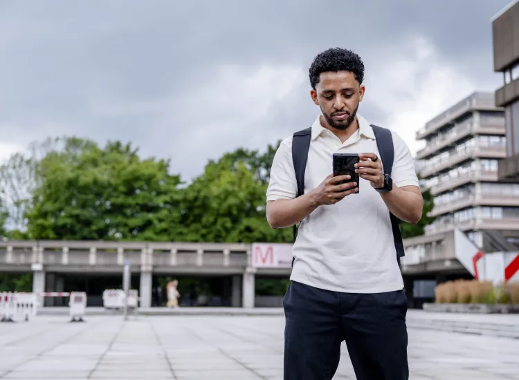 Ein Student steht mit seinem Smartphone in der Hand auf dem Campusgelände der RUB.