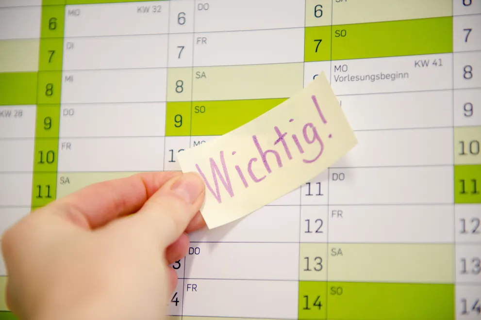 Hand klebt Post-it mit Aufschrift Wichtig auf einen Kalender.
