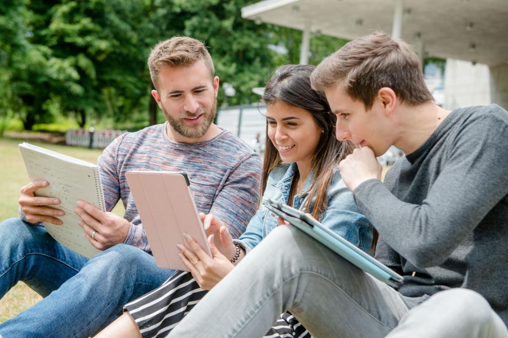 Drei Studierende sehen sich auf dem RUB-Campus Inhalte auf einem Tablet an.