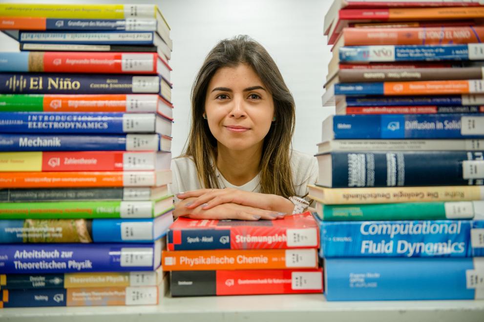 Eine Studierende über einem Stapel Bücher.