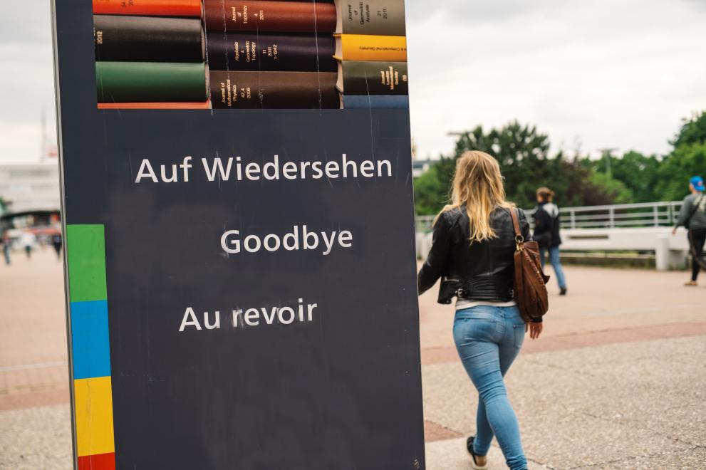 Studentin am Schild "Auf Wiedersehen/Goodbye/Au revoir" auf der Unibrücke"