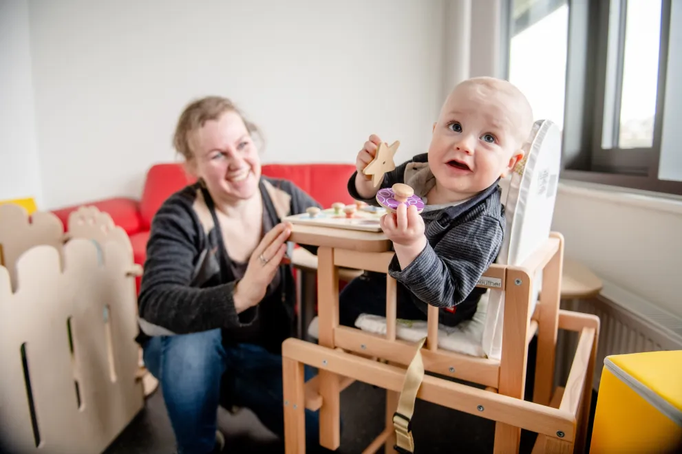 Mutter spielt mit Kind im Hochstuhl. 
