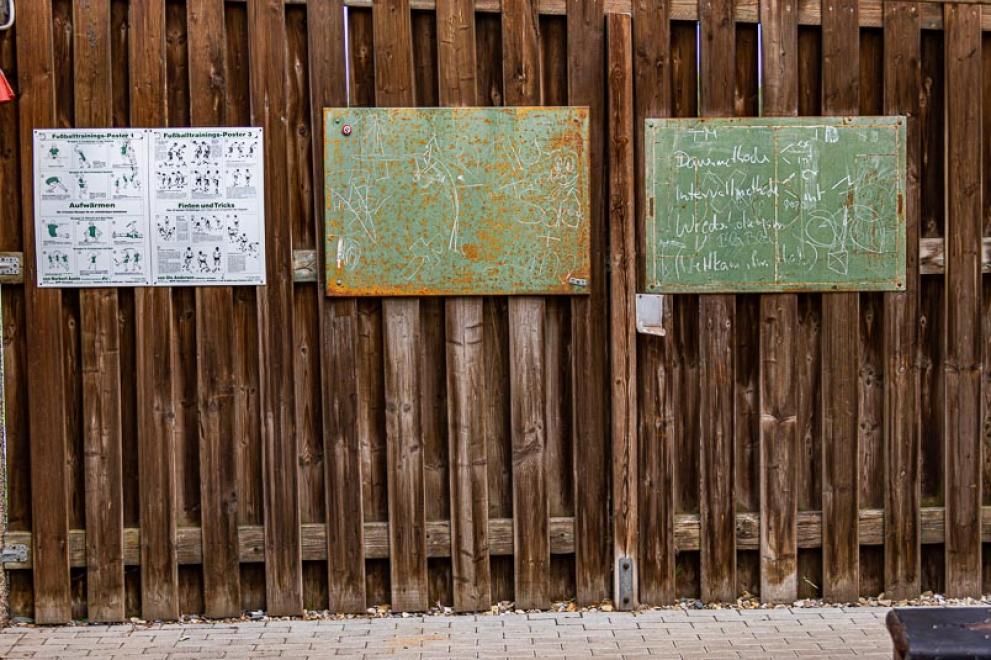 Das Foto zeigt einen Holzzaun mit Schildern, auf denen historische Übungsanleitungen zu sehen sind.
