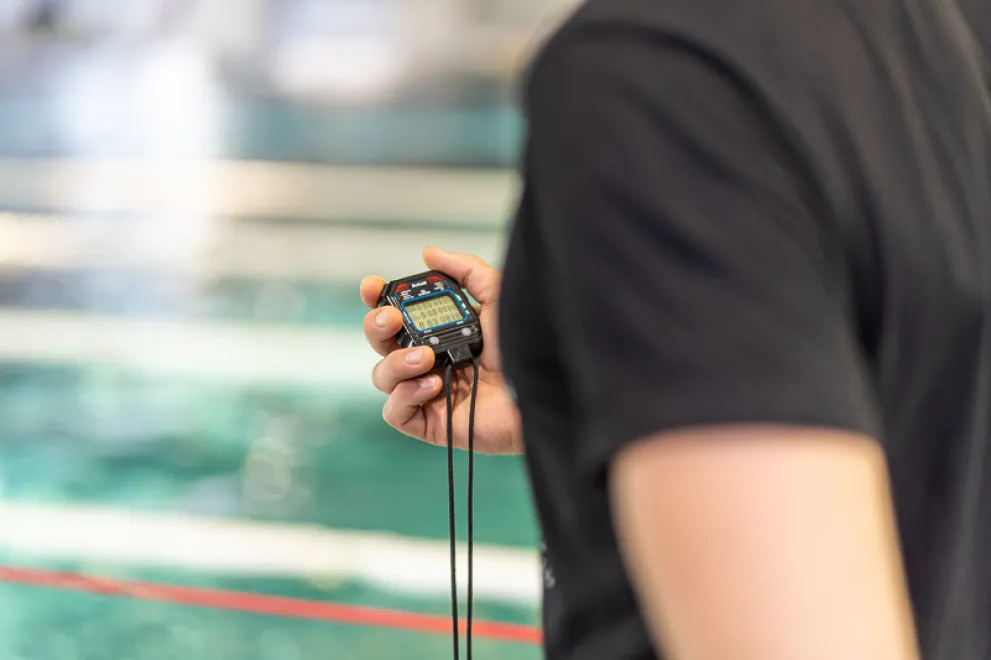 Am Rand eines Schwimmbeckens stoppt ein Mann mit einer Stoppuhr die Zeit.