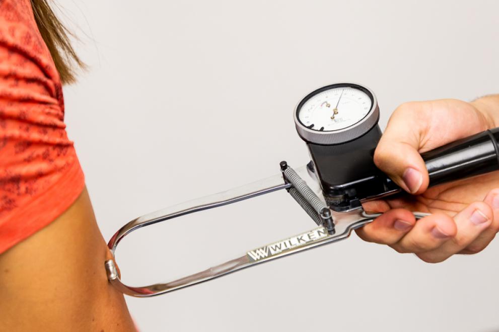 Bei einer jungen Frau wird mit einem Diagnoseinstrument der Körperfettanteil am Oberarm gemessen