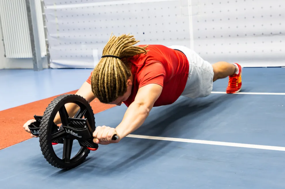 Foto: Ein junger Mann hält sich beim Liegestütz an den Griffen eines Rollers fest, mit dem seine Kraft gemessen wird.