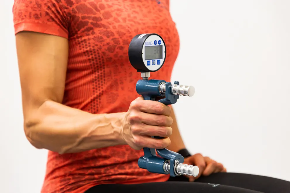 Foto: Eine junge Frau hält mit angewinkeltem Arm ein Gerät, um ihre Kraft zu messen