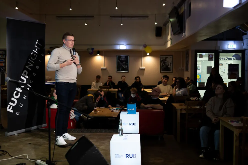 Mann steht mit Mikrofon auf Bühne