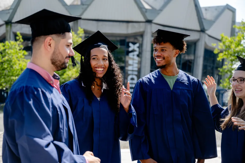 Mehrere Personen mit Abolsventenhüten stehen vor dem Audimax der Ruhr-Universität Bochum und unterhalten sich.
