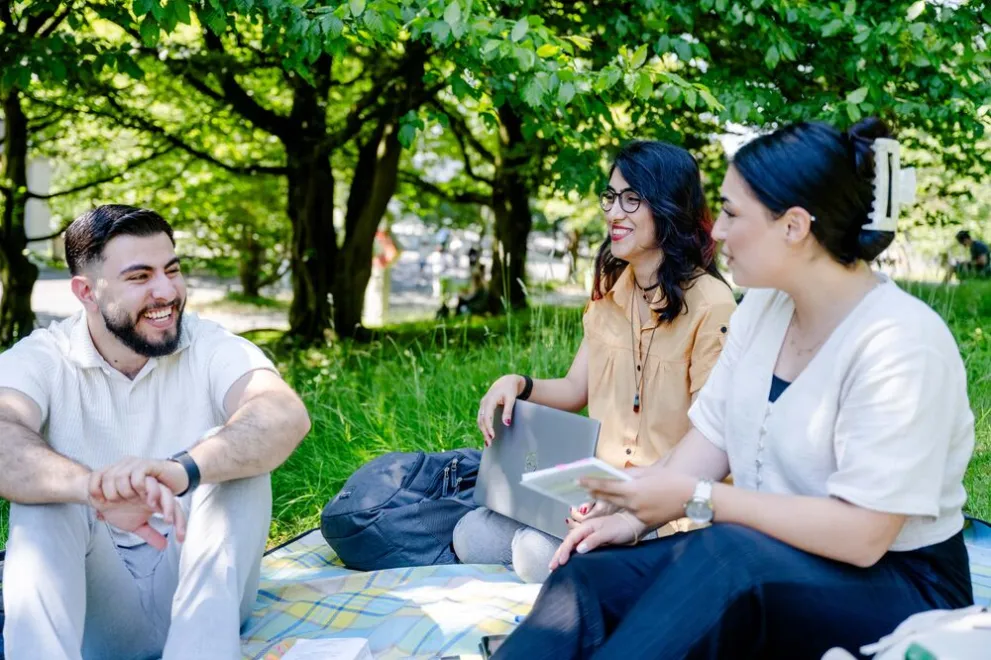 Drei junge Menschen sitzen auf einer Wiese und unterhalten sich