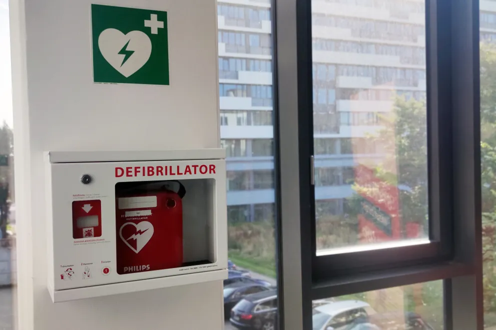 Defibrillator an der Wand in einem RUB-Gebäude, gekennzeichnet mit einem Icon, das Weiß auf Grün ein Herz mit einem Blitz-Symbol zeigt.