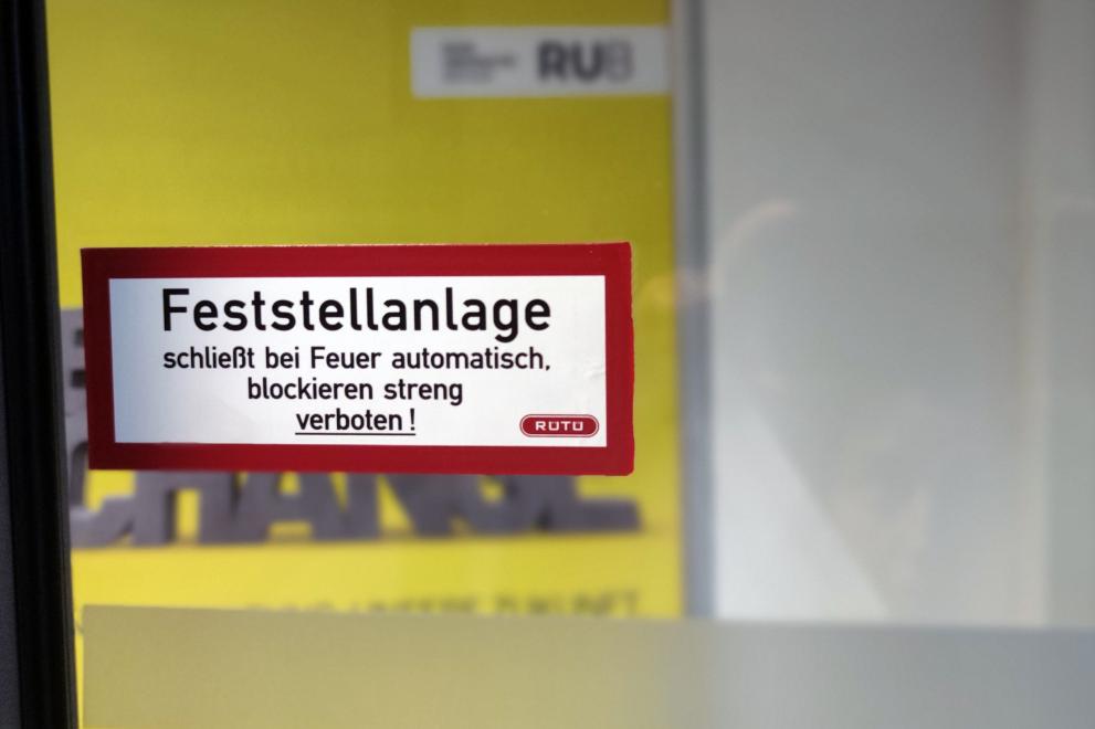 Glastür mit Aufkleber "Feststellanlage schließt bei Feuer automatisch, blockieren streng verboten1"