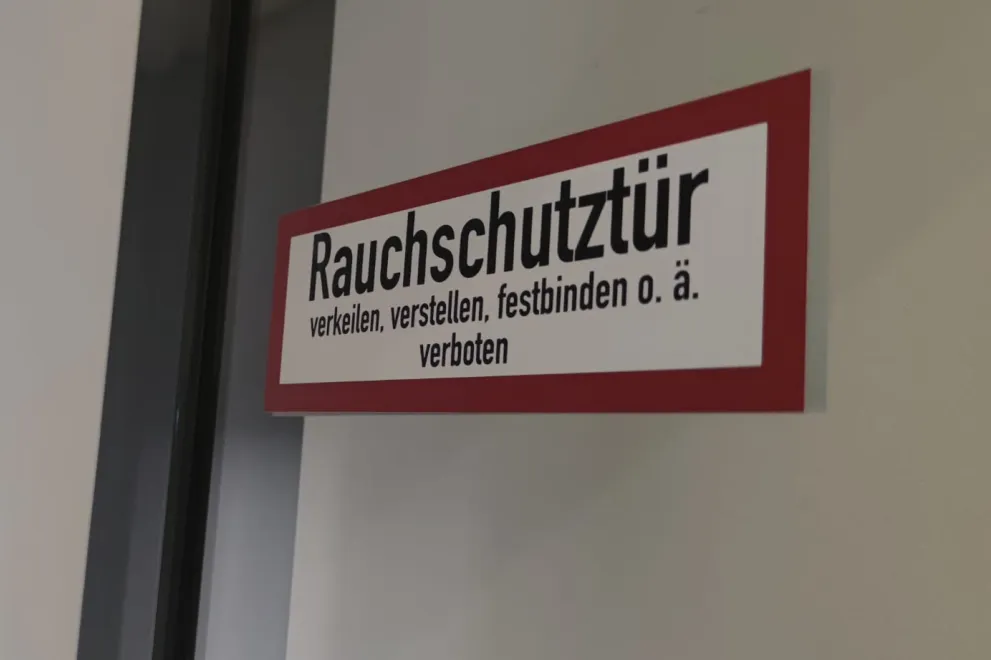 Der Hinweisaufkleber an einer Tür mit dem Hinweis „Rauchschutztür. verkeilen, verstellen, festbinden o. ä. verboten